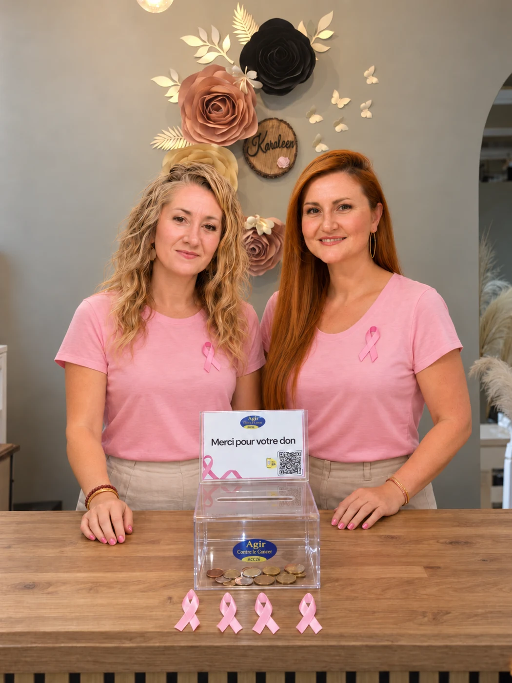 Line et Caroline portant le ruban rose, près de l’urne de dons ACC26 à l’Institut Karoleen